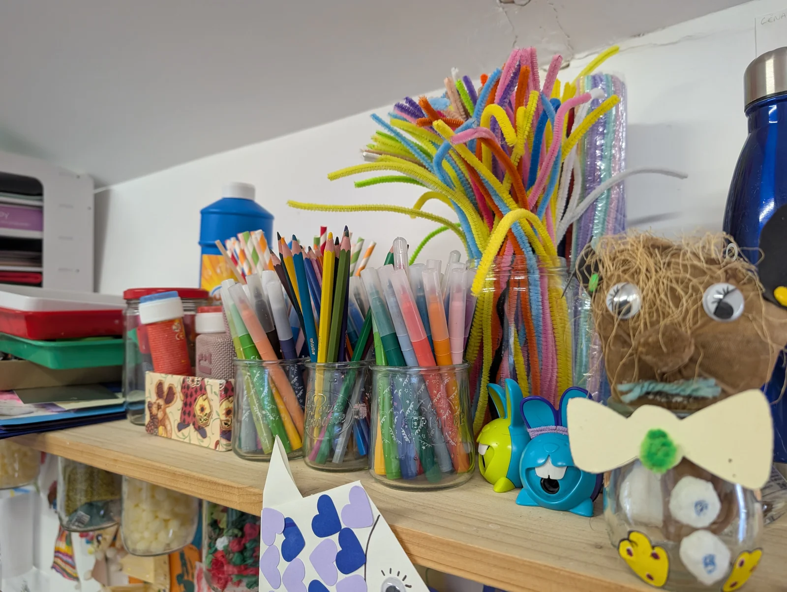 Étagère du local : crayons, feutres et cure-pipes dans des pots en verre
